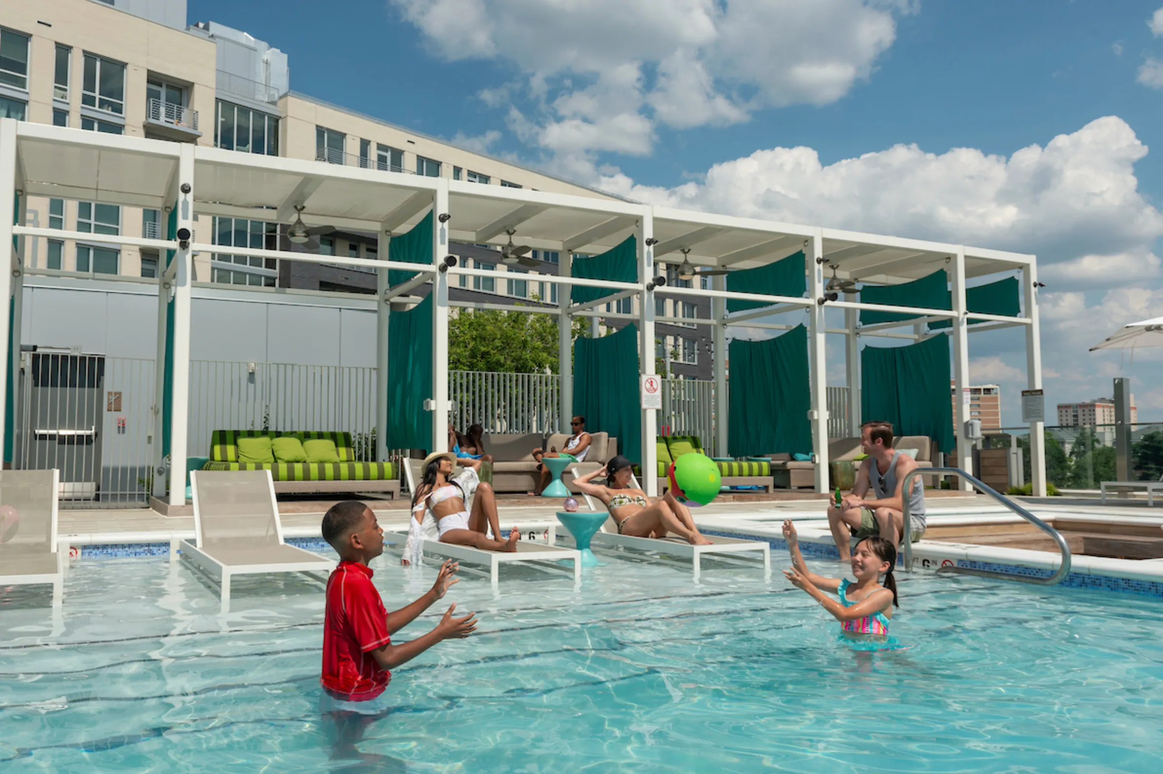boy and girl playing in a pool with two women laying on lounge chairs behind them