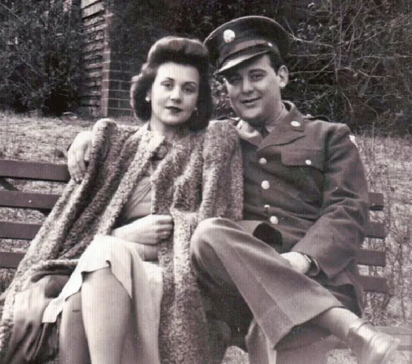 black and white image of a man in an Army uniform sitting next to a woman on a bench