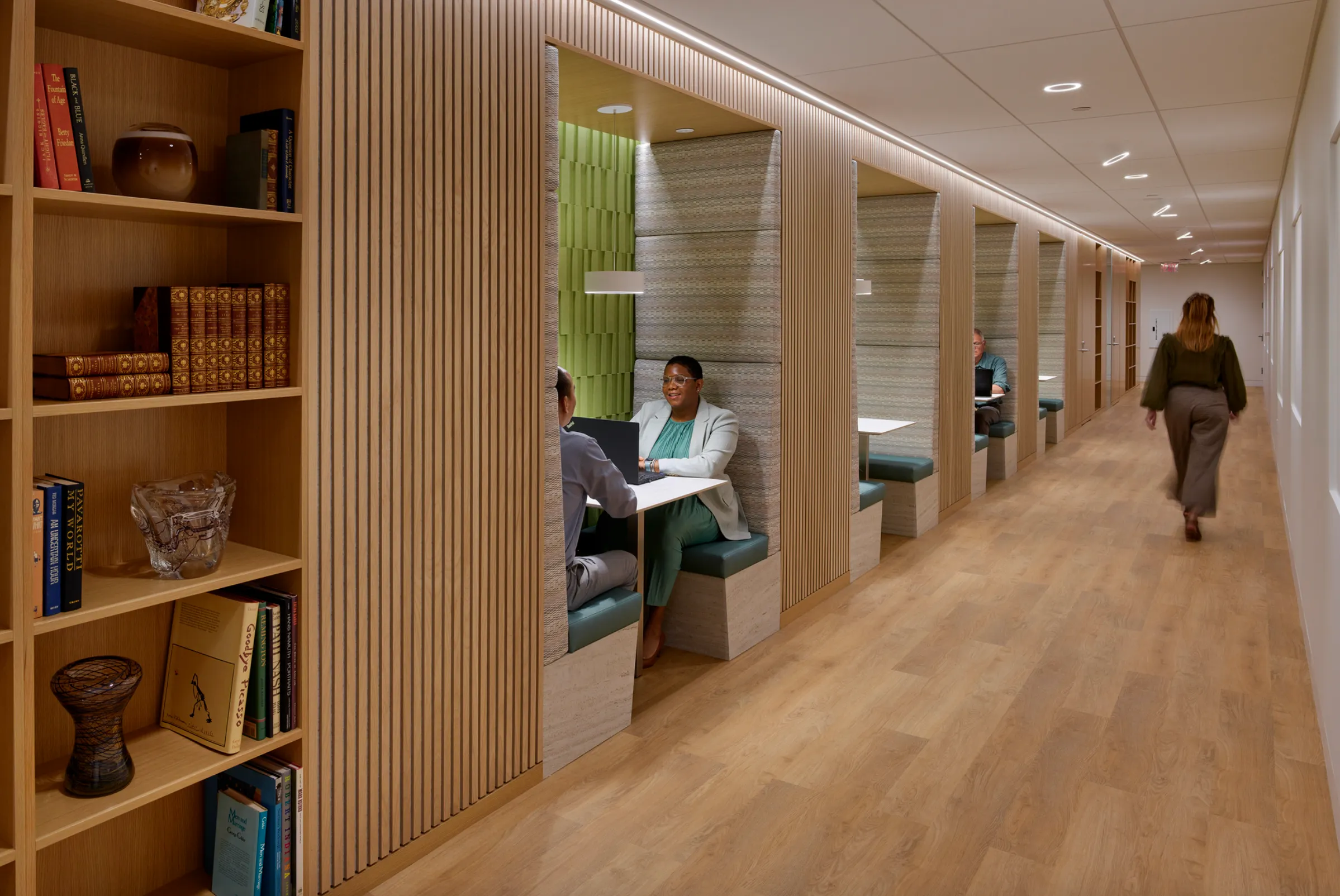 two people sitting in a booth and a woman walking down the hall next to them