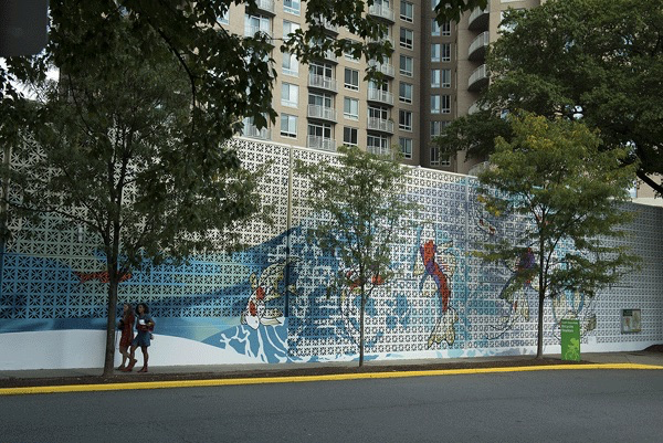 trees along a sidewalk in front of a wall with a fish mural painted on it
