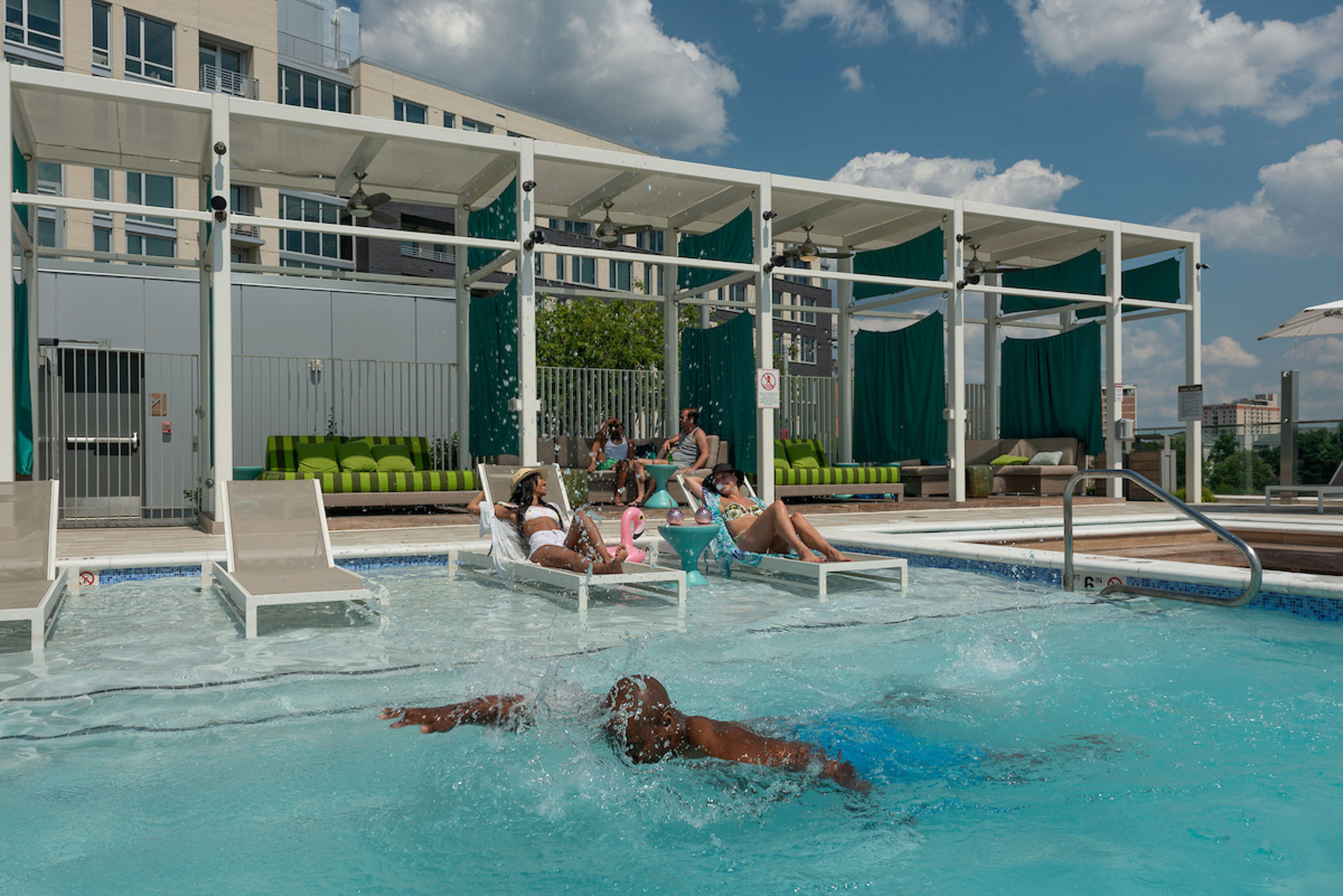 man swimming in pool with two women laying on lounge chairs behind him